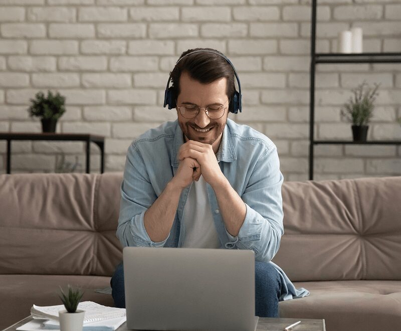 A man sitting on the couch with headphones on his ears.