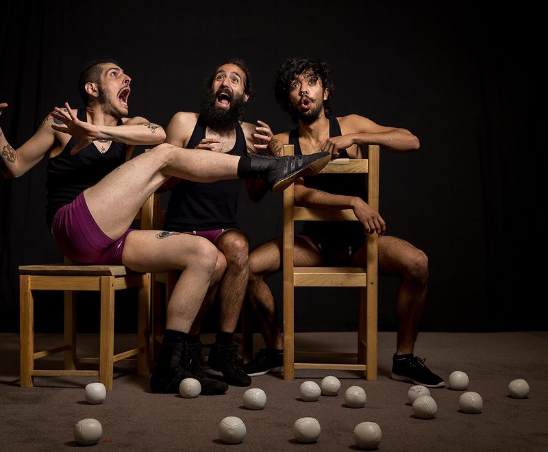 Three men sitting in chairs with balls on the floor.