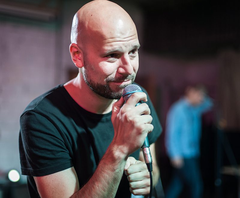 A bald man with a shaved head is holding a microphone.